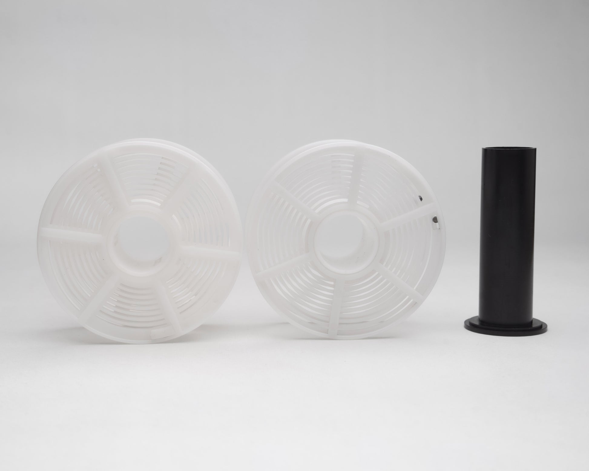 Two white plastic film developing reels and a black cylindrical object on a light gray background